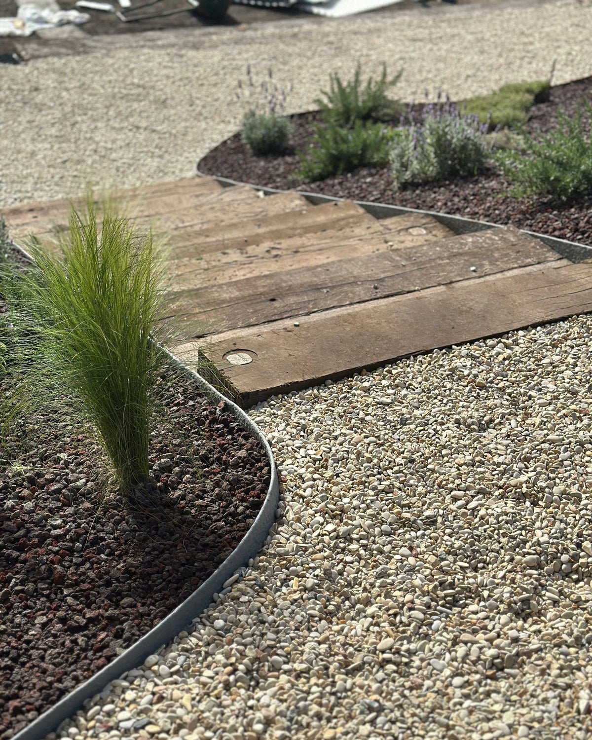 Dettaglio percorso in ghiaia con bordo curvo e pedana in legno, design giardino AbitoVerde