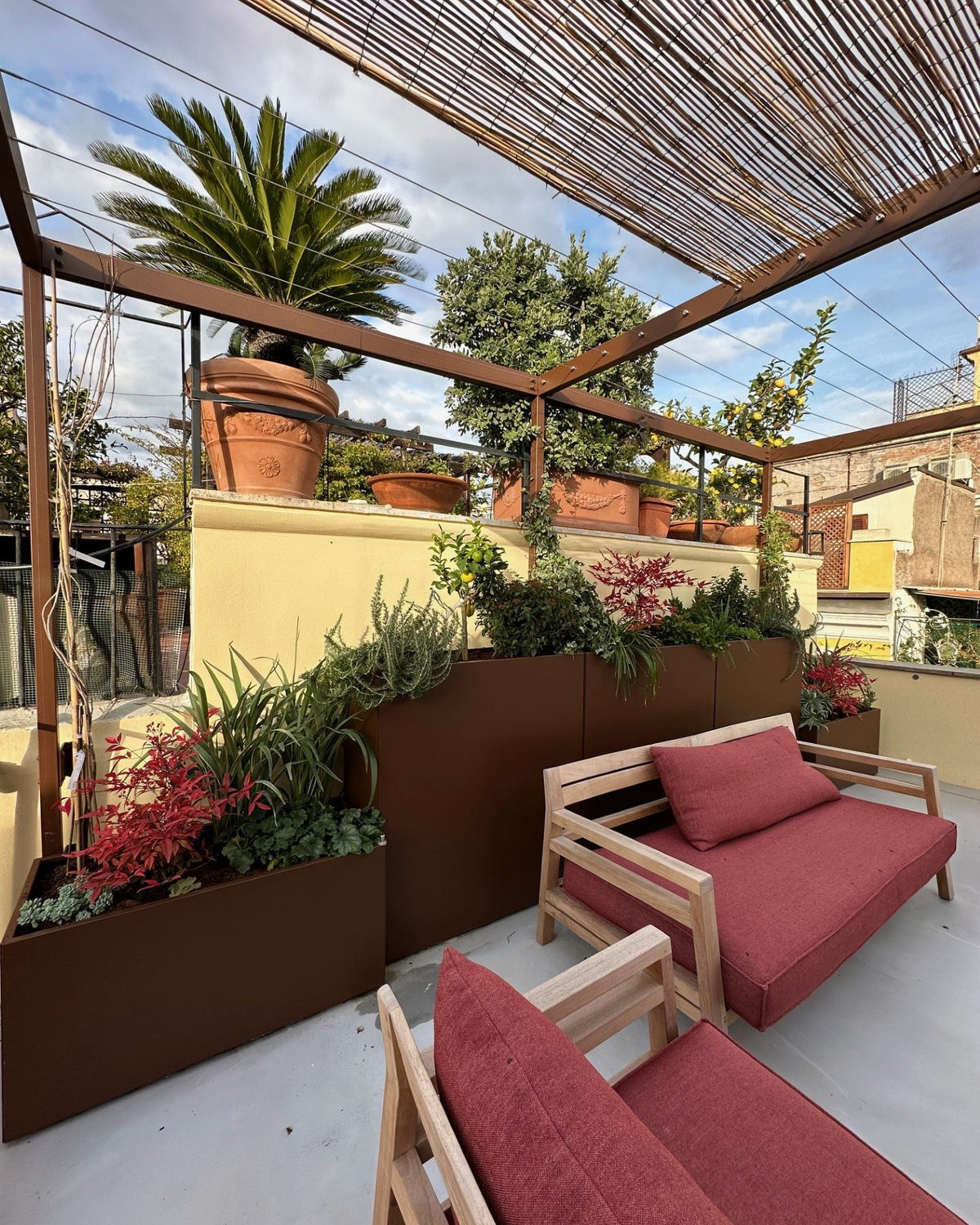 Zona relax terrazza Boschetto con divani rossi e vasi corten piante verdi, design AbitoVerde