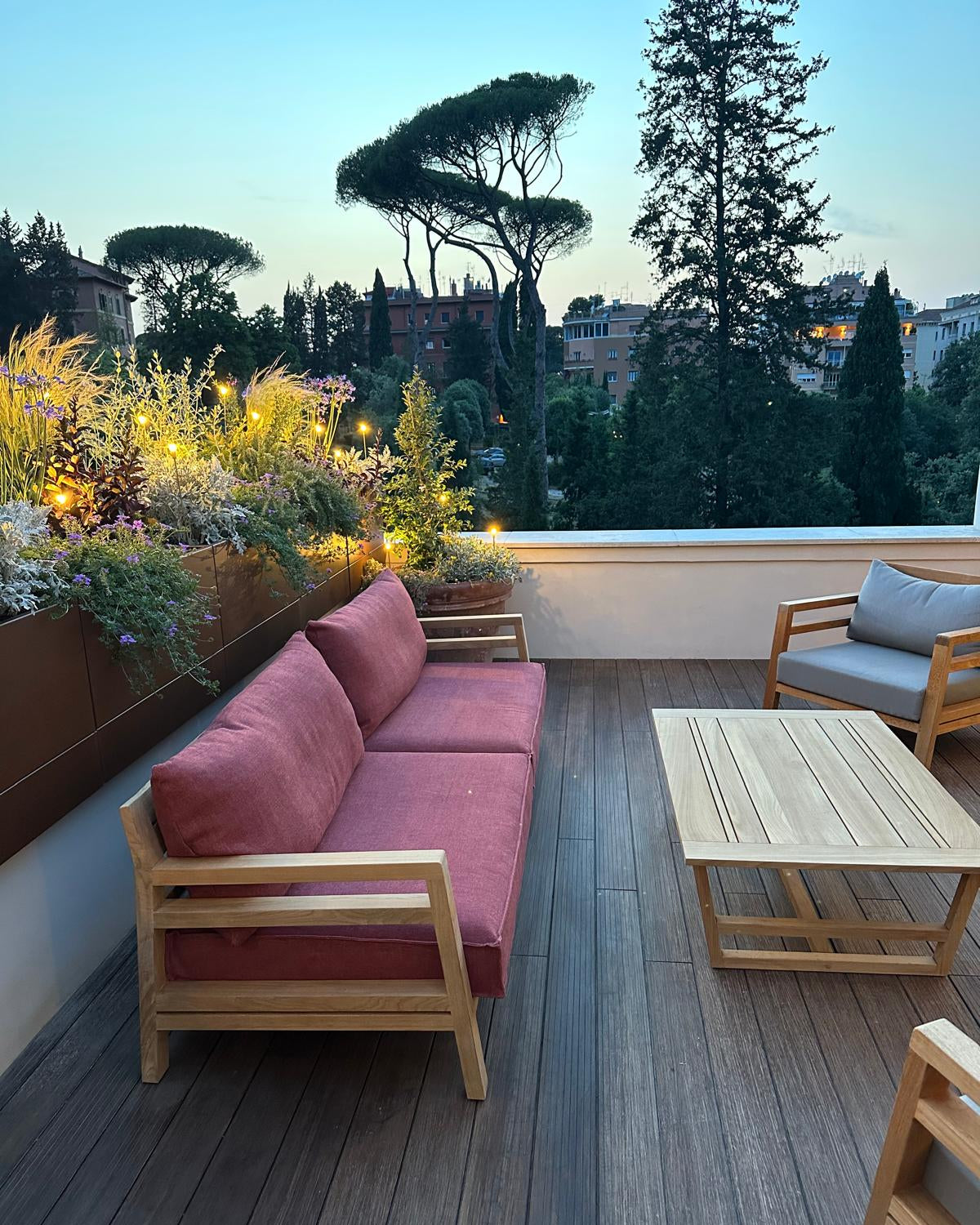 Zona relax terrazza Novella con divani rossi, tavolo legno e piante alte fiorite AbitoVerde