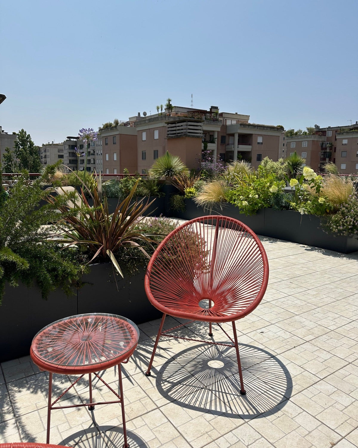 Sedia rossa design terrazza Torrino con vista edifici Roma e piante fiorite AbitoVerde